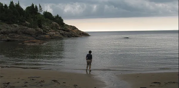 Person standing alone on deserted beach on overcast day